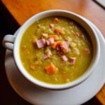 Close-up of a thick, green pea soup topped with diced ham and carrots.