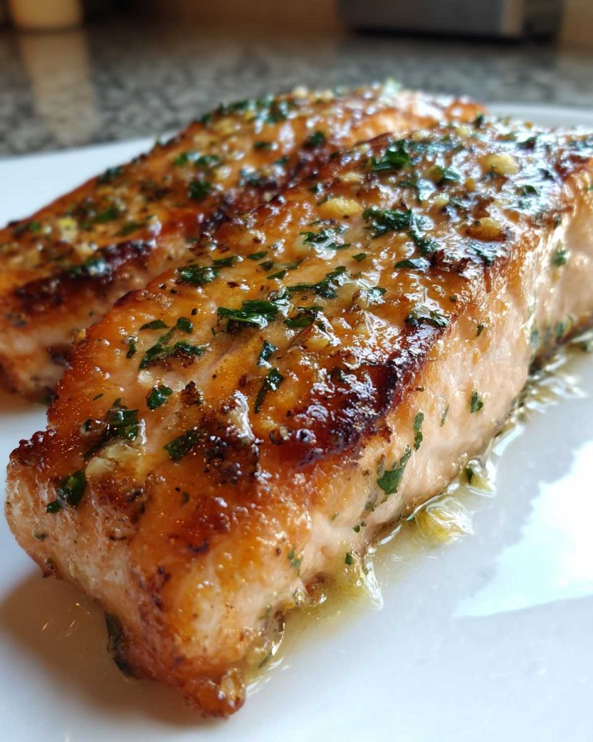 Close-up of two perfectly cooked air fryer salmon fillets glistening with a garlic butter glaze and fresh parsley.