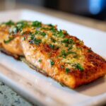 A close-up of a perfectly cooked fillet of air fryer salmon topped with garlic and fresh parsley.