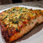 Close-up of a flaky, golden-brown air fryer salmon fillet topped with green herbs.