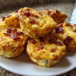 A stack of five golden brown bacon egg bites served on a small white plate.