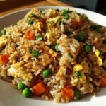 A close-up, appetizing shot of homemade chicken fried rice mixed with scrambled egg, bright green peas, and diced carrots.