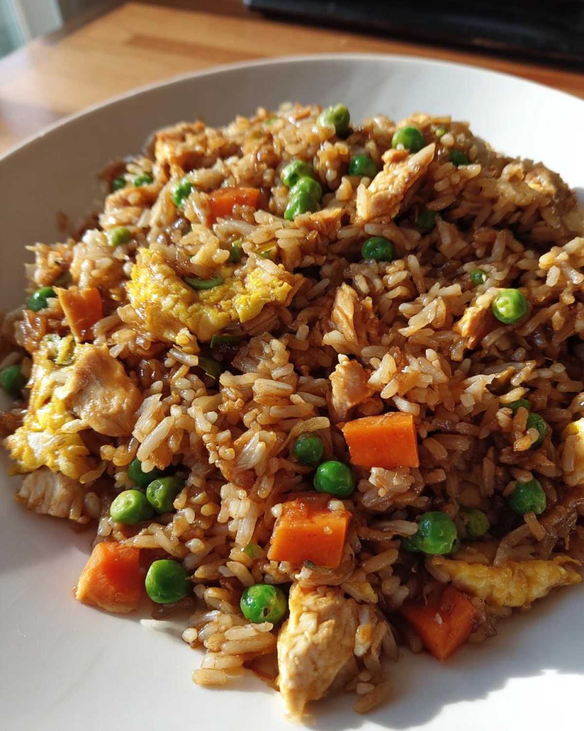 A close-up serving of amazing chicken fried rice mixed with diced carrots, green peas, and scrambled egg pieces.