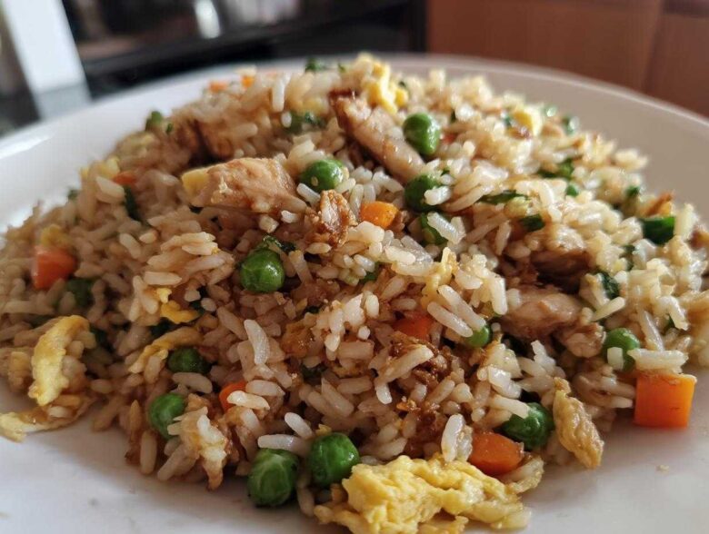 A close-up serving of amazing chicken fried rice featuring white rice, chunks of chicken, peas, carrots, and scrambled egg.