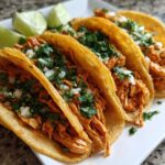 Four delicious, vibrant orange chicken tacos topped with cilantro and onion, served with lime wedges.
