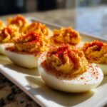 Close-up of perfectly piped deviled eggs garnished with bright red paprika on a white platter.