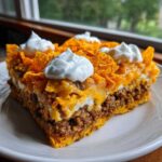 A hearty slice of Dorito Casserole featuring layers of seasoned ground beef, melted cheese, and crushed chips topped with dollops of sour cream.