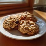 Three golden brown oatmeal cookie treats piled on a white plate, illuminated by sunlight.
