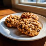 Three freshly baked oatmeal cookie treats resting on a white plate near a sunlit window.