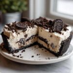 A slice removed from an amazing Oreo pie showing the creamy filling, dark crust, and cookie crumbles on top.