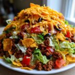 A towering plate of amazing taco salad featuring seasoned ground beef, lettuce, tomatoes, olives, cheese, and crushed tortilla chips.