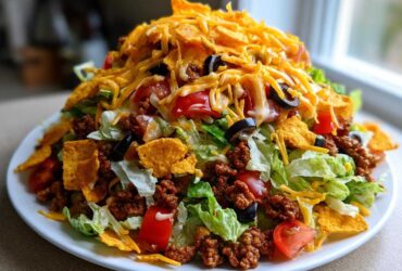 A towering plate of amazing taco salad featuring seasoned ground beef, lettuce, tomatoes, olives, cheese, and crushed tortilla chips.