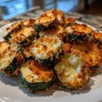 A pile of crispy, golden brown baked parmesan zucchini slices topped with melted cheese.