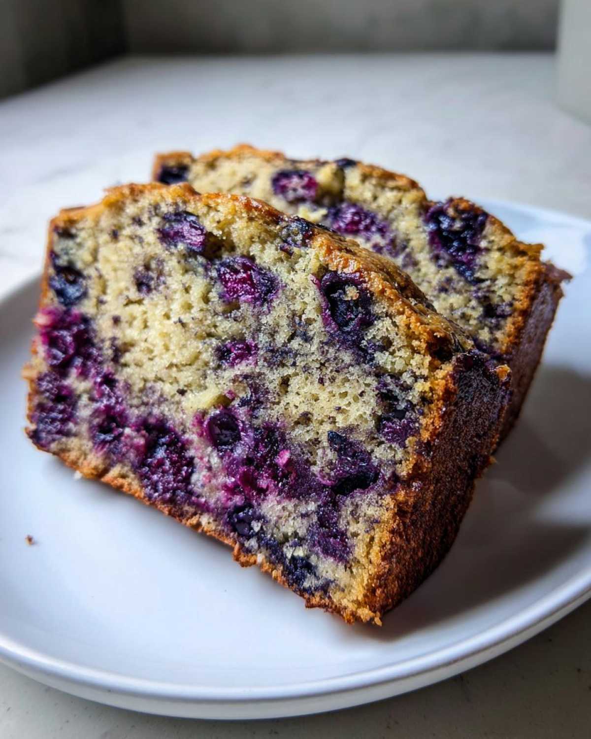 Close-up of two moist slices of blueberry banana bread showing vibrant purple blueberries baked into the crumb.
