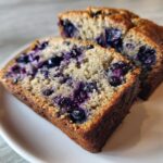 Close-up of two thick slices of moist blueberry banana bread showing vibrant purple blueberries throughout the crumb.