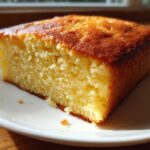 A close-up shot of a thick, golden slice of buttermilk cornbread resting on a white plate.