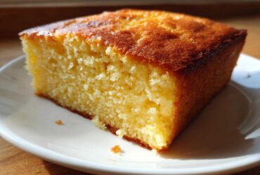 A close-up shot of a thick, golden slice of buttermilk cornbread resting on a white plate.