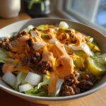 A close-up of a delicious cheeseburger bowl featuring ground beef, lettuce, pickles, onions, cheese, and special sauce.