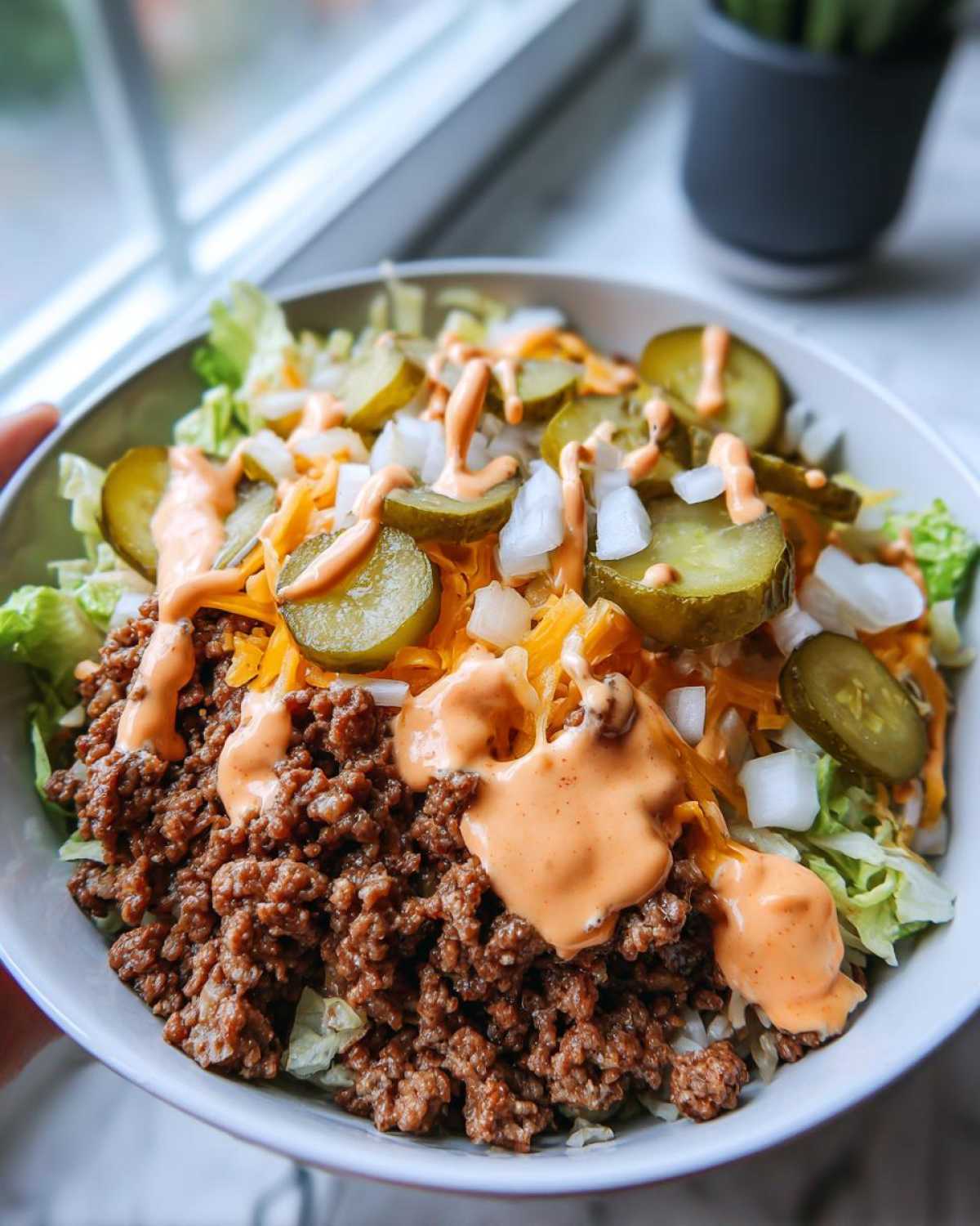 A close-up view of a cheeseburger bowl featuring seasoned ground beef, shredded lettuce, cheese, pickles, and special sauce.