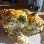A serving of cheesy broccoli rice casserole being lifted with a fork, showing melted cheese strings.
