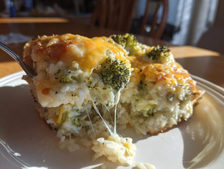 A serving of cheesy broccoli rice casserole being lifted with a fork, showing melted cheese strings.