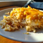 Close-up of a serving of cheesy chicken and rice casserole with melted cheddar cheese on top.