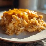 A close-up serving of creamy, cheesy chicken and rice casserole topped with melted cheddar cheese.