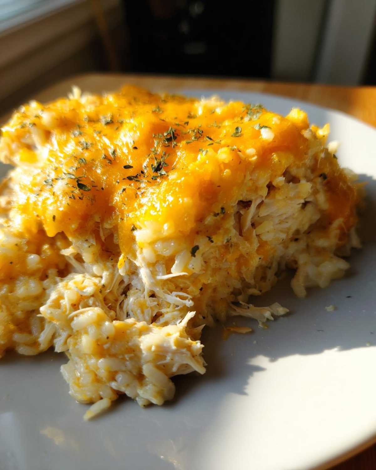Close-up of a serving of cheesy chicken and rice, topped with melted cheddar and herbs.