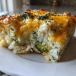 A square slice of baked chicken broccoli rice casserole topped with melted cheddar cheese.