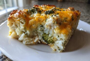 A square slice of baked chicken broccoli rice casserole topped with melted cheddar cheese.