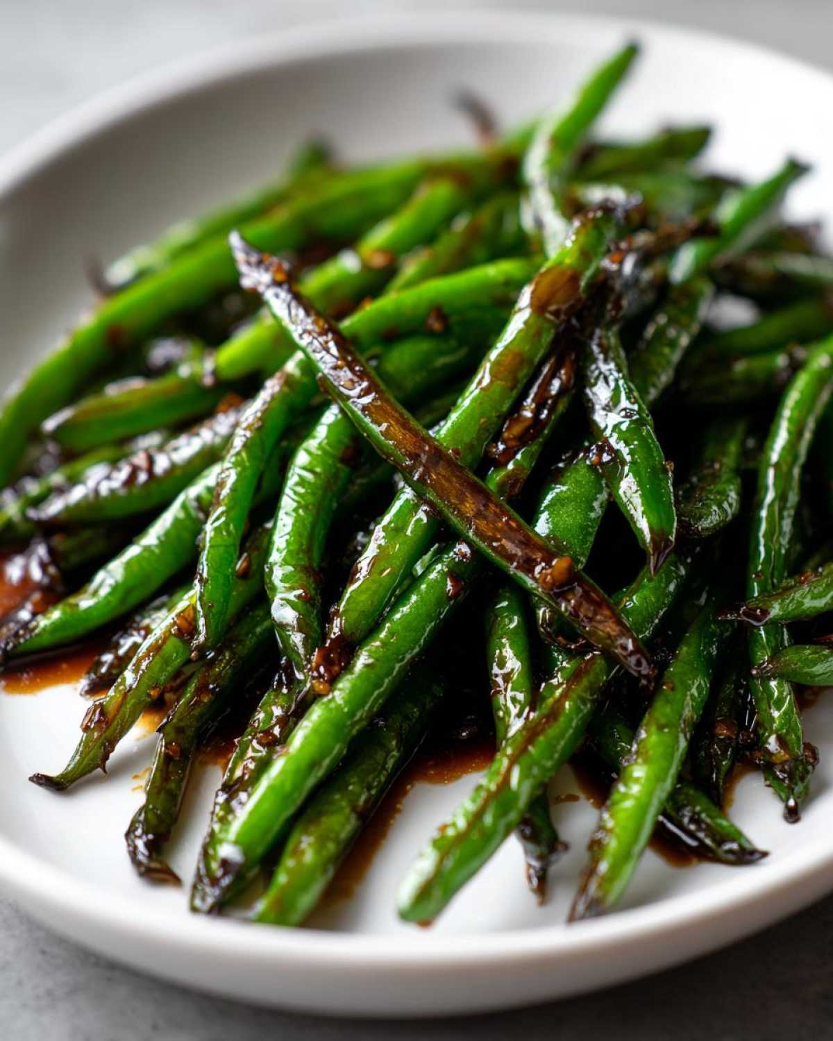 Close-up of vibrant, blistered chinese green beans with garlic sauce coating them in a white bowl.