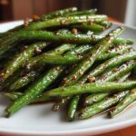 Close-up of vibrant green beans coated in a glossy, dark garlic sauce, ready to serve.