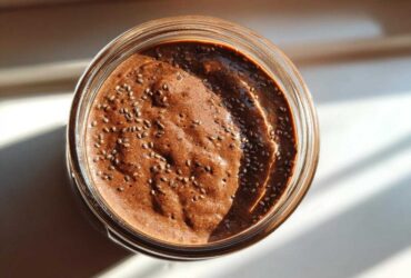 Overhead view of rich chocolate overnight oats topped with chia seeds in a glass jar, illuminated by sunlight.