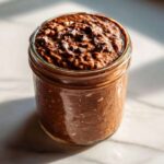 Close-up of rich chocolate overnight oats topped with chocolate chips in a glass jar.