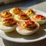 A white plate holding six creamy, perfectly piped deviled eggs, generously dusted with bright red paprika.