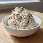 A scoop of creamy cottage cheese chicken salad mixed with red onion and dill, served in a white bowl.