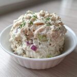 A scoop of creamy cottage cheese chicken salad mixed with red onion and celery, garnished with dill, served in a white bowl.