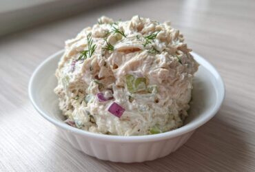 A scoop of creamy cottage cheese chicken salad mixed with red onion and celery, garnished with dill, served in a white bowl.