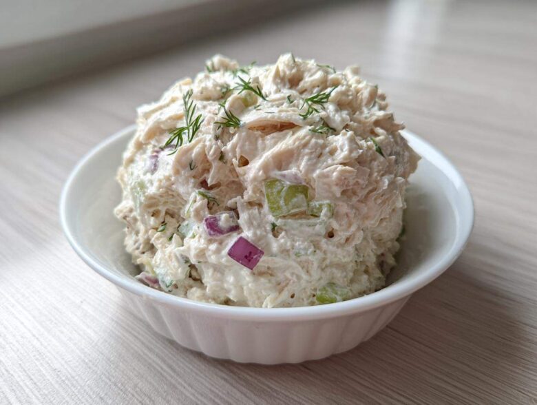 A scoop of creamy cottage cheese chicken salad mixed with red onion and celery, garnished with dill, served in a white bowl.
