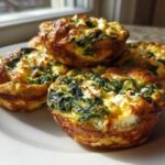 A close-up of four golden-brown Cottage Cheese Egg Cups With Spinach & Feta stacked on a white plate.