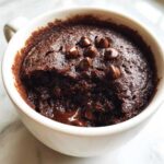 Close-up of a rich, dark Cottage Cheese Microwave Brownie topped with chocolate chips inside a white mug.
