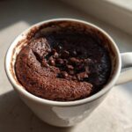 A rich, dark chocolate Cottage Cheese Microwave Brownie baked in a white mug, topped with chocolate chips.