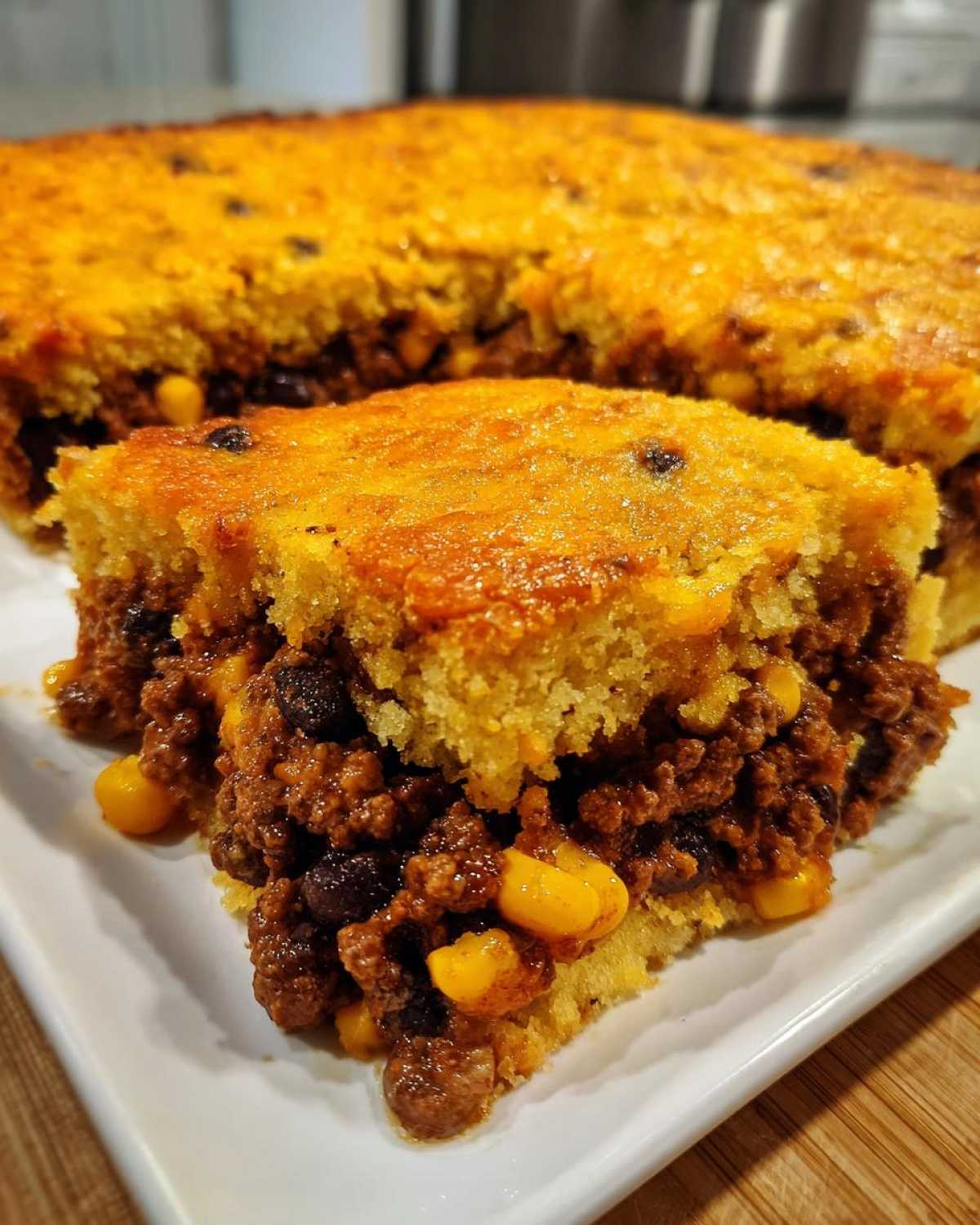 A slice of cowboy cornbread casserole showing a thick, savory meat and bean filling topped with golden cornbread.
