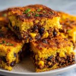Close-up of stacked squares of cowboy cornbread casserole showing the savory ground meat, corn, and bean filling between the cornbread layers.