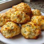A pile of freshly baked cream cheese sausage balls topped with melted cheddar cheese and parsley on a white plate.