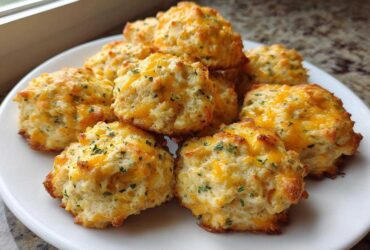 A pile of freshly baked cream cheese sausage balls topped with melted cheddar cheese and parsley on a white plate.