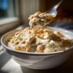 A spoonful of creamy crockpot white chicken chili being lifted from a white bowl.