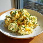 A generous serving of creamy egg salad recipe, chunky with egg pieces and topped with finely chopped green chives.