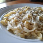 Close-up of fettuccine pasta generously coated in creamy homemade alfredo sauce and sprinkled with herbs.