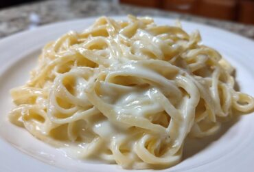 Close-up of fettuccine pasta generously coated in rich, creamy homemade alfredo sauce on a white plate.